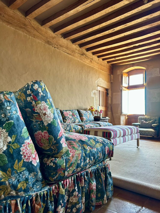 Floral-patterned sofa in a room with wooden beams and large windows.